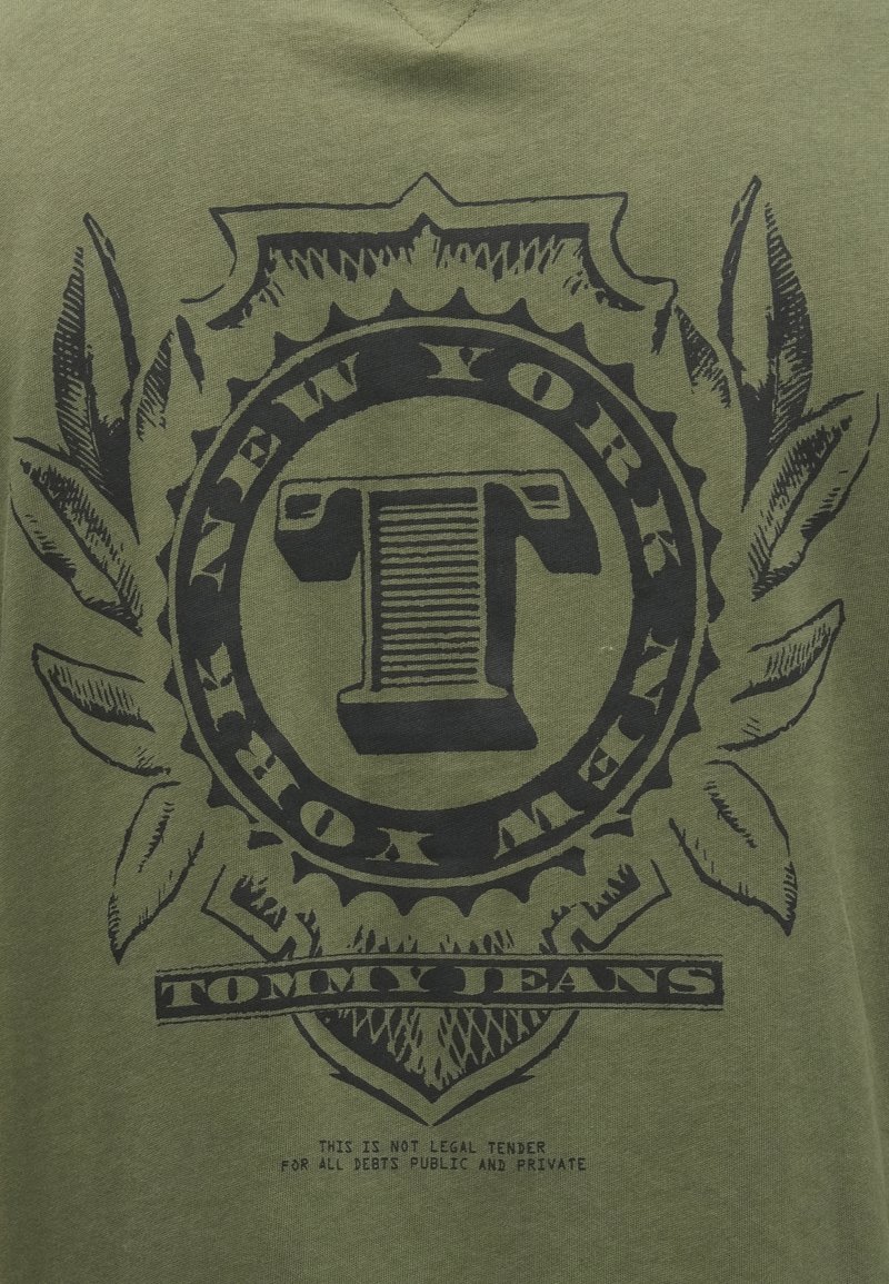 Grön bomulls T-shirt med en svart grafisk design, inklusive ett cirkulärt emblem med texten "NEW YORK" och "TOMMY JEANS" samt bladaccent.