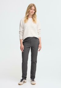 Grå byxor med slim fit och lite stretch, kombinera med en ljus texturerad tröja och beige skor med mörka ränder.