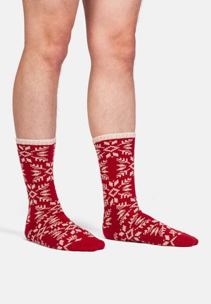 Calze rosse di lana con un risvolto crema che presenta un motivo a fiocco di neve su tutta la superficie. La texture sembra morbida e accogliente, adatta per il freddo.