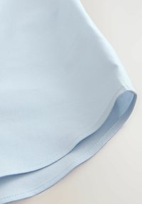 Tessuto azzurro chiaro con una texture liscia, orlo curvo e cuciture pulite. Il materiale sembra leggero e traspirante.