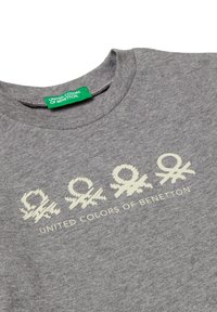 Šedé bavlněné tričko s grafickým designem se čtyřmi stylizovanými symboly ve světlé smetanové barvě a textem "UNITED COLORS OF BENETTON" pod ním.