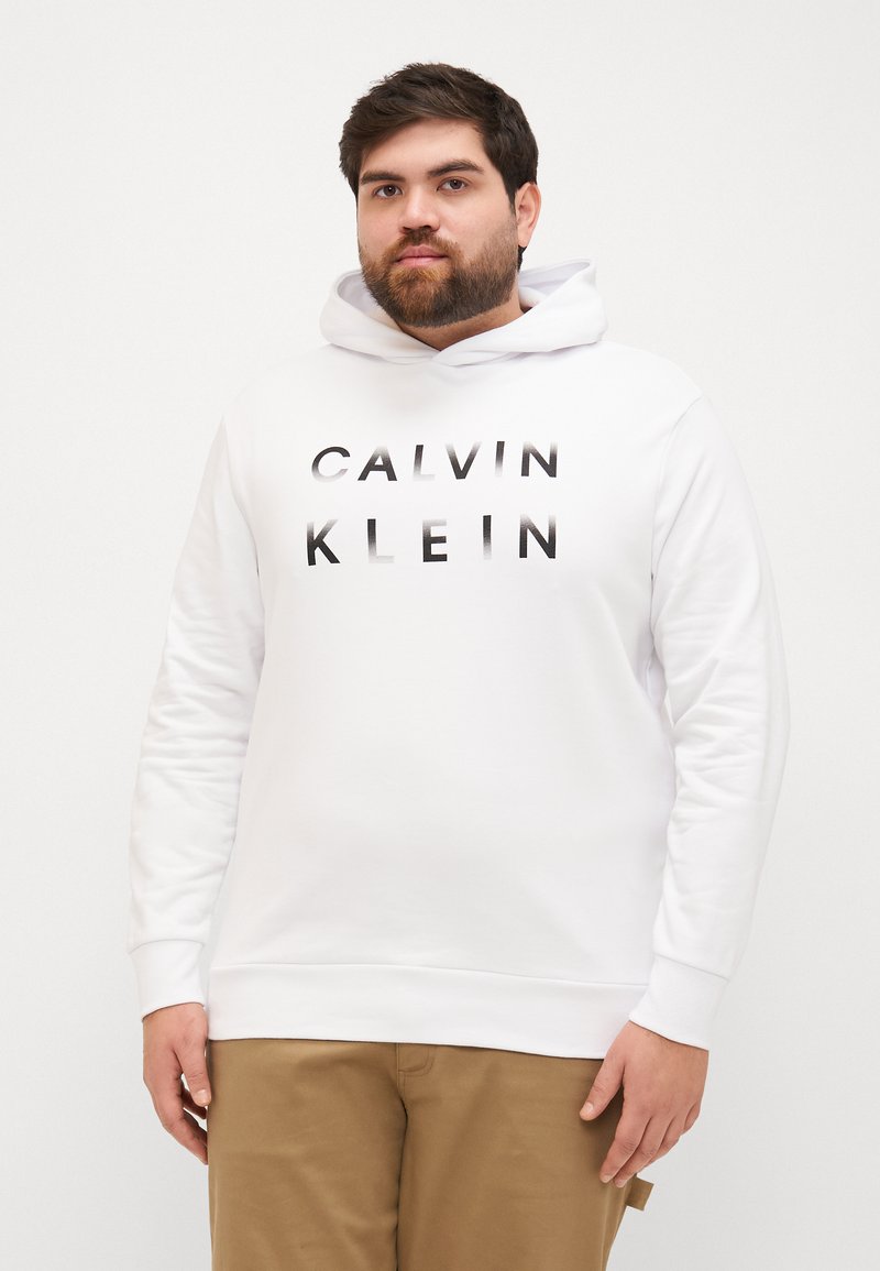 Biała bluza z kapturem wykonana z bawełnianego materiału, z przednią kieszenią typu kangura, ściągaczami przy mankietach oraz logo "CALVIN KLEIN" w czarnym napisie.