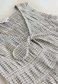 Kohvipruuni ja kreemika ruudulise mustriga tekstuurse kangaga top, taljel lipsuga ja V-kaelusega.