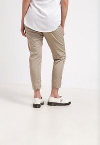 Světle béžové kalhoty se slim fit střih, zúženými kotníky a hladkou texturou. Oděny s bílými botami s detaily přezky.