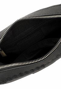 Intérieur d'un sac en cuir noir avec une fermeture éclair argentée, une poche intérieure zippée, et des détails de couture le long du bord de l'ouverture du sac.