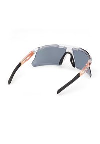 Okulary przeciwsłoneczne sportowe z przezroczystą oprawką, szarymi szkłami oraz czarnymi gumowymi zausznikami z teksturowanym uchwytem i pomarańczowym akcentem na zausznikach.