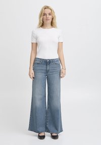 Top corto a maniche corte bianco a righe abbinato a jeans in denim blu a vita alta e gamba larga, caratterizzati da una texture liscia e da un leggero effetto sbiadito.