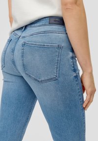 Dunne blauwe jeans met een klassiek vijf-pocket ontwerp, vervaagde textuur en een subtiele logopatch op de achterste tailleband.