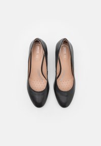 Paire de ballerines pour femmes en cuir noir à bout rond avec semelles intérieures rembourrées portant la mention "GEOX Respira" sur fond blanc.