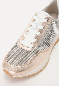 Rosenvergoldete Sneaker mit Mesh-Design, weißen Schnürsenkeln und grauen Akzenten. Besitzt einen Seitenreißverschluss und eine strukturierte Sohle für besseren Halt.