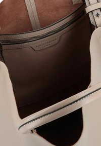 Be�żowa skórzana torebka wewnątrz o gładkiej fakturze, z kieszenią na zamek i miękkim brązowym wykończeniem. Widoczne charakterystyczne detale przeszycia.