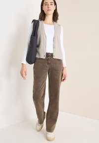 Hellgrau gestrickte Weste mit gerippten Kanten, weißes Langarmshirt, braune Cordhosen und lässige Sneaker mit strukturierten Details.