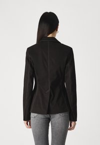 Svart blazer med skreddersydd passform, notched lapels og kontrasterende hvit søm. Baksiden har en sømdesign og lange ermer.