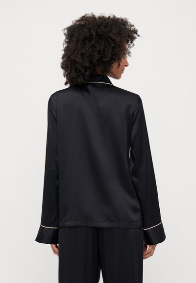 Black satin pajama shirt featuring long sleeves, a classic collar, and pale piping along the cuffs and collar. Smooth texture and relaxed fit.