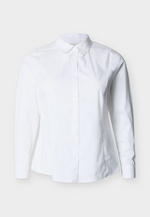 Fehér, hosszú ujjú, gombos ing hegyes gallérral és testhezálló derékrésszel, világos háttér előtt.