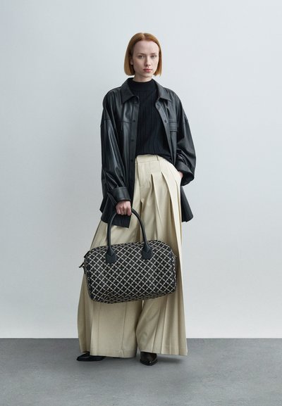 Καφέ μαύρο δερμάτινο πουκάμισο μεγάλης διάστασης, μαύρο ριμπ πουλόβερ, μπεζ πλισέ παντελόνια και μια υφασμάτινη μαύρη και μπεζ τσάντα με σχέδιο.