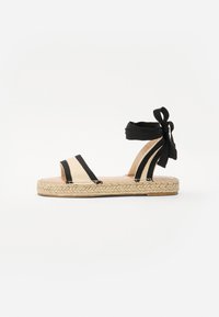 Sandală espadril cu degetele deschise, neagră și bej, având talpă din iută împletită și cravate la gleznă. Design în dungi cu o textură netedă.