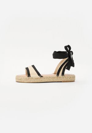 Černé a béžové espadrilové sandály s otevřenou špičkou, s tkanou jutu podrážkou a šněrováním kolem kotníku. Pruhovaný design s hladkým povrchem.