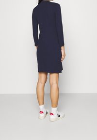 Mörkblå klänning med lång ärm och rak skärning, med sidoflikar, i kombination med vita sneakers och ankelsockor. Mjukt tyg, minimalistisk design.