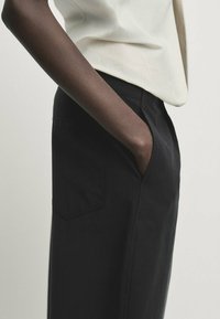 Czarne, dopasowane spodnie o prostym kroju, z bocznymi kieszeniami i lekkiego materiału. Połączone z kremową bluzką. Minimalistyczny design.