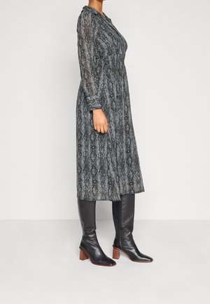 Kvinde iført en langærmet, grå midi-kjole med slangeprint, sat sammen med sorte læderstøvler til knæet med blokhæle.