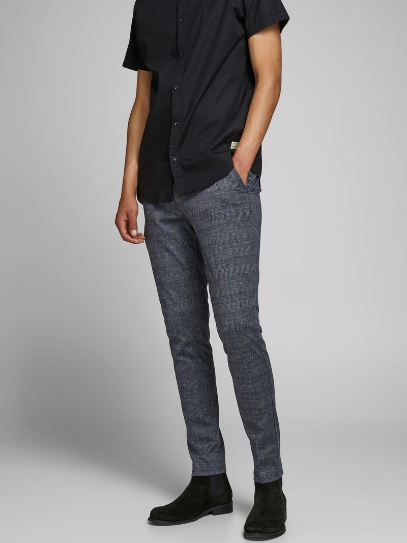 Pantalons à carreaux bleu marine avec un design slim-fit, tissu texturé et poches latérales, associés à une chemise noire à manches courtes et des bottines noires.