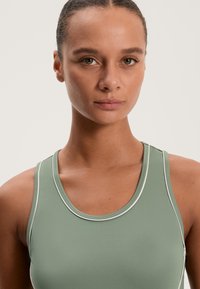 Zöld sportos ujjatlan felső fehér díszítéssel, kerek nyakkivágással és sima felülettel, aktív viseléshez tervezve.