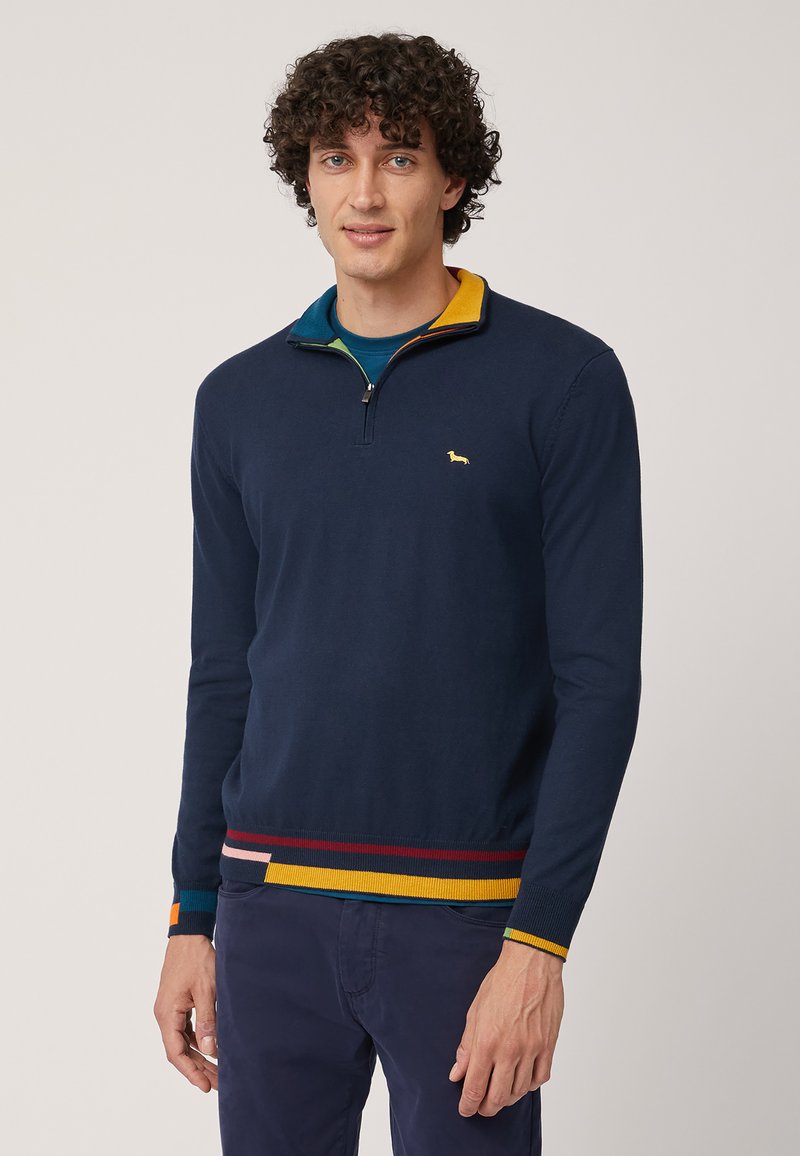 Maglione a collo zip di colore blu navy con orlo a righe multicolore. Presenta un piccolo logo giallo sul petto. Texture morbida.