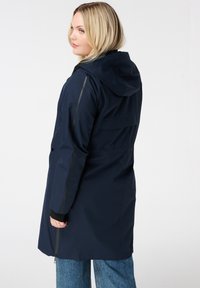 Marine waterdichte jas met capuchon, met zijritsen, gestructureerde stof en accentstrepen langs de mouwen. Middellange uitvoering.