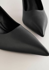 Mustat korkokengät, jotka on valmistettu sileästä nahasta, kärjessä terävä muoto ja minimalistinen design, matala leikkuuvaha ja ilman näkyvää metalliosaa.