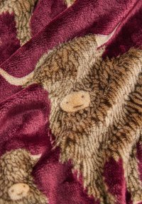 Fleece blanket featuring a burgundy background with detailed, textured illustrations of shaggy brown highland cows.