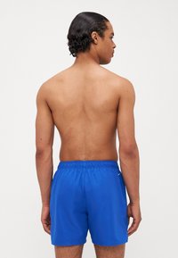 Shorts de bain bleus en matériau léger, avec une taille élastique et des coutures latérales, offrant une texture lisse et un branding minimal.