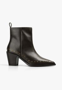 Botín de cuero negro hasta el tobillo con punta afilada, tachuelas de bronce decorativas a lo largo del lateral y un tacón robusto. Presenta un lazo de tirón en la parte posterior.