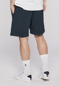 Navy blue cotton shorts with side pockets and an elastic waistband, paired with white ribbed socks and white sneakers with a black heel accent.
