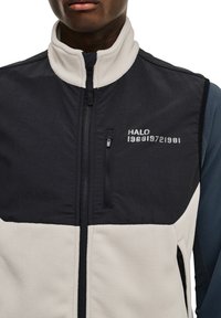 Fleeceväst i marinblått och krämvitt, med hög krage, dragkedja framtill och broderad detalj "HALO 1968|1972|1981" på bröstet.