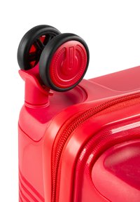 Valigia rigida rossa con superficie testurizzata, accenti scanalati e ruote nere. Include un tasto prominente per il funzionamento.