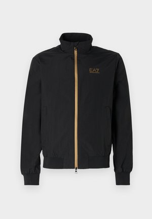 Black bomber jacket made from smooth fabric. Features a high collar, gold zipper, and EA7 logo on the left chest. Elastic cuffs and hem.