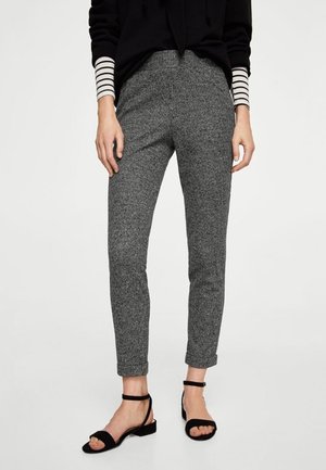Personne portant un pantalon slim gris texturé, des sandales noires à bride à la cheville, un top noir et une chemise à manches longues rayée en dessous.