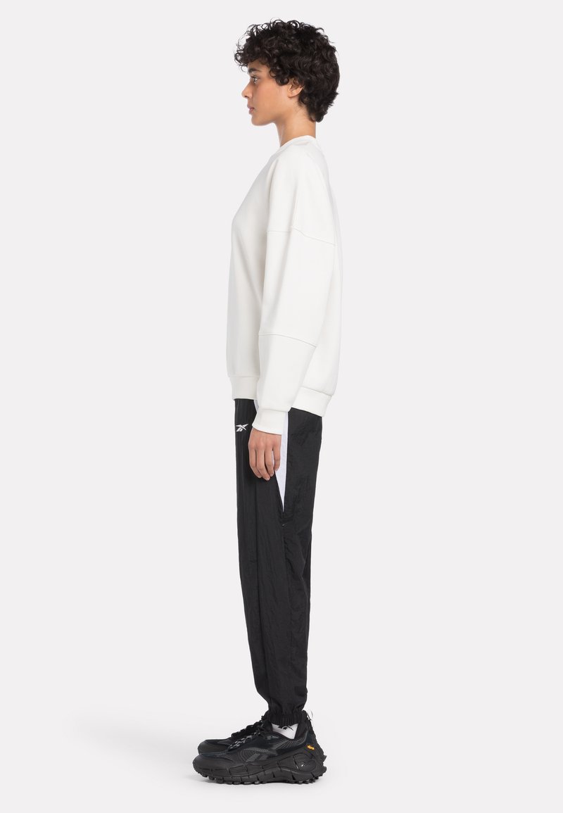 Weißer übergroßer Sweatshirt, schwarze taillierte Hose mit weißen Akzenten und klobigen schwarzen Turnschuhen. Glatter Stoff, lockere Passform und elastische Bündchen.