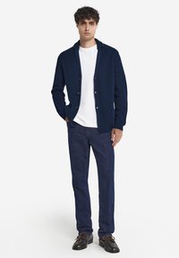 Marinblå stickad cardigan med sjalkrage, med framknäppning och fickor, kombinerad med slim fit mörkblå byxor och svarta skor.