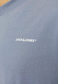 Svetlomodré bavlnené tričko s okrúhlym výstrihom a bielym logom "JACK&JONES" potlačeným na hrudi. Tkanina má hladkú štruktúru.