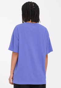Camiseta de algodón morada con un corte relajado, mangas cortas y un escote redondo, que presenta un dobladillo recto y detalles de costura mínimos.