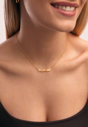 Krupan plan žene koja se smiješi, nosi zlatni lančić s riječju "mama" i privjeskom u obliku srca na crnoj majici.