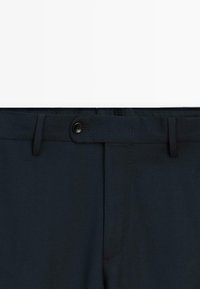 Mörkblå byxor med knappstängning, slim fit-design och subtil textur, med snyggt avslutade sömmar och inga synliga mönster.
