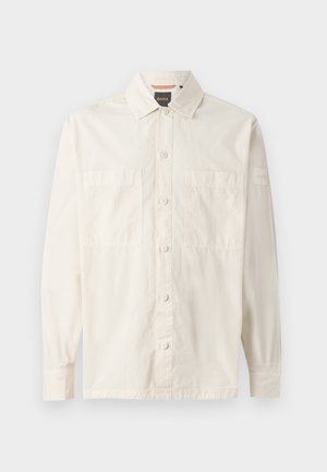 Beige langemouwshirt van lichtgewicht stof, met een knoopsluiting aan de voorkant, twee borstzakken en een merklabel op de mouw.