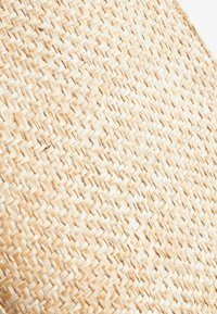 Gros plan d'une texture en paille tissée beige montrant des fibres naturelles entrelacées en motif diagonal.