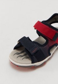 Marineblau und rote Kindersandale mit verstellbaren Riemen, perforiertem beigen Fußbett und Krallenmuster auf der Sohle, ausgestattet mit einem leichten Design.