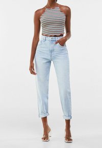 Gestreepte cropped top met een afgeronde halslijn in meerdere kleuren. Lichtblauwe hoge taille jeans met opgerolde pijpen. Transparante sandalen met hak.