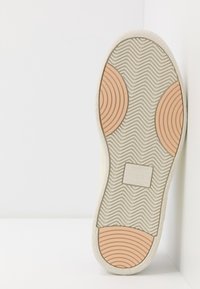 Podeszwa buta z falistym wzorem teksturalnym, o jasnoszarej podstawie i dwóch okrągłych pomarańczowych akcentach w pobliżu pięty.