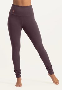 Hochgeschnittene Leggings aus einem dunkelvioletten Stoff, mit gerafften Knöcheln und einem kontrastierenden gestickten Logo am Bund.